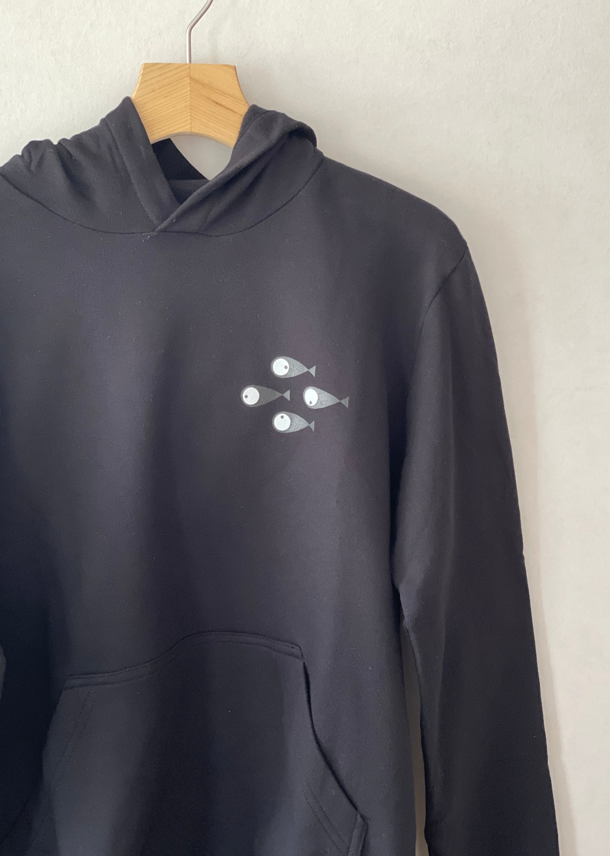 Super cozy hoodie with a kangaroo pocket in the front with no drawstrings. Crafted from 100 % superfine cotton. Raglan sleeves, ribbed trims. The pieces have a pink fish print on front left bottom corner and 4 black fishes print on right chest side. Colour: black Material: 100% cotton