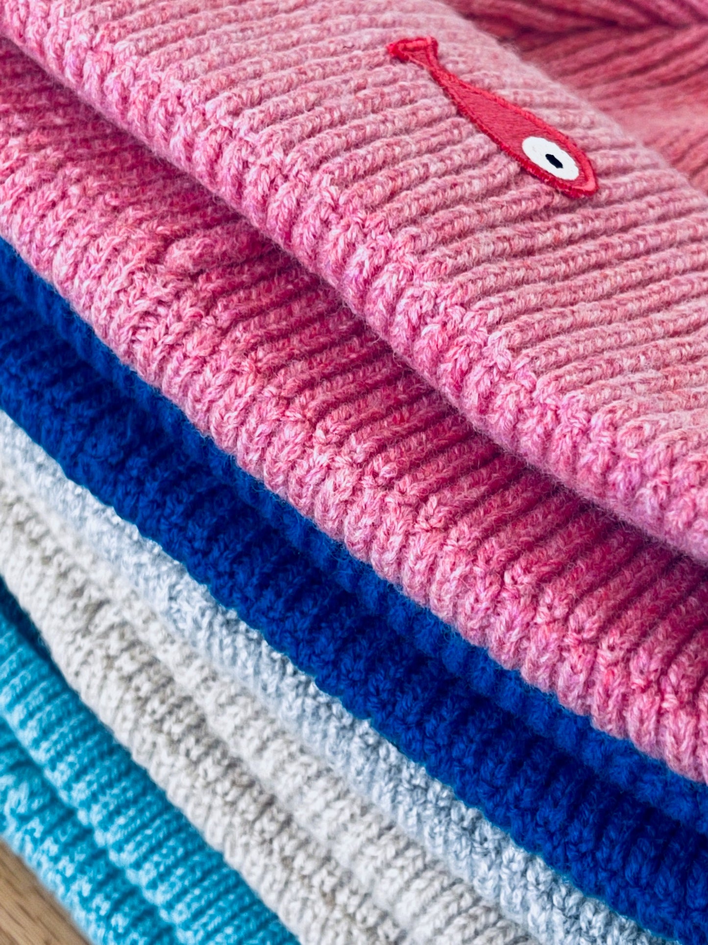 The collection of soft, colorful, and warm beanies crafted from luxurious lambswool yarn. Embrace comfort and style with these lovely accessories available in four captivating colors: Pink, Blue, Vibrant Mint, and Light Grey. Each beanie features a unique fish patch, adding a touch of charm and playfulness.  Detail
