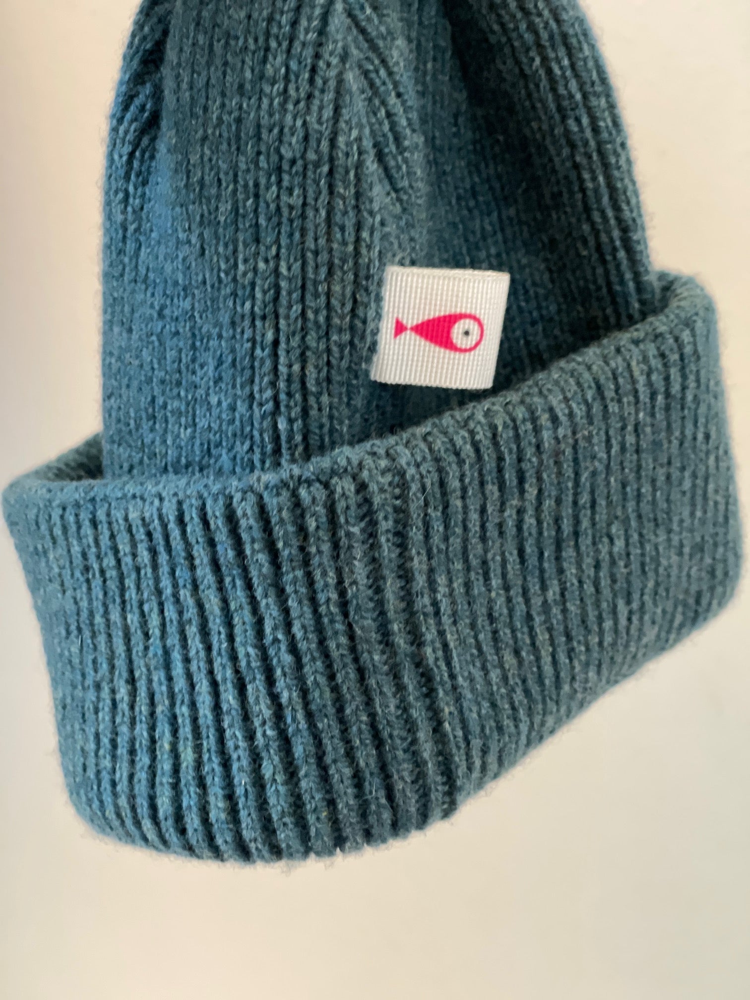 The soft, colorful, and warm kids/baby beanies crafted from luxurious lambswool yarn.   Adorned with a playful fish patch for a touch of playfulness. ( The Turquoise color features a distinctive back label. The front of the label showcases a pink fish, turn the label around, and you'll find our logo discreetly placed on the back )  Vibrant palette of seven colors – Yellow, Purple, Red, Blue, Pink, Navy Blue and Turquoise. Front