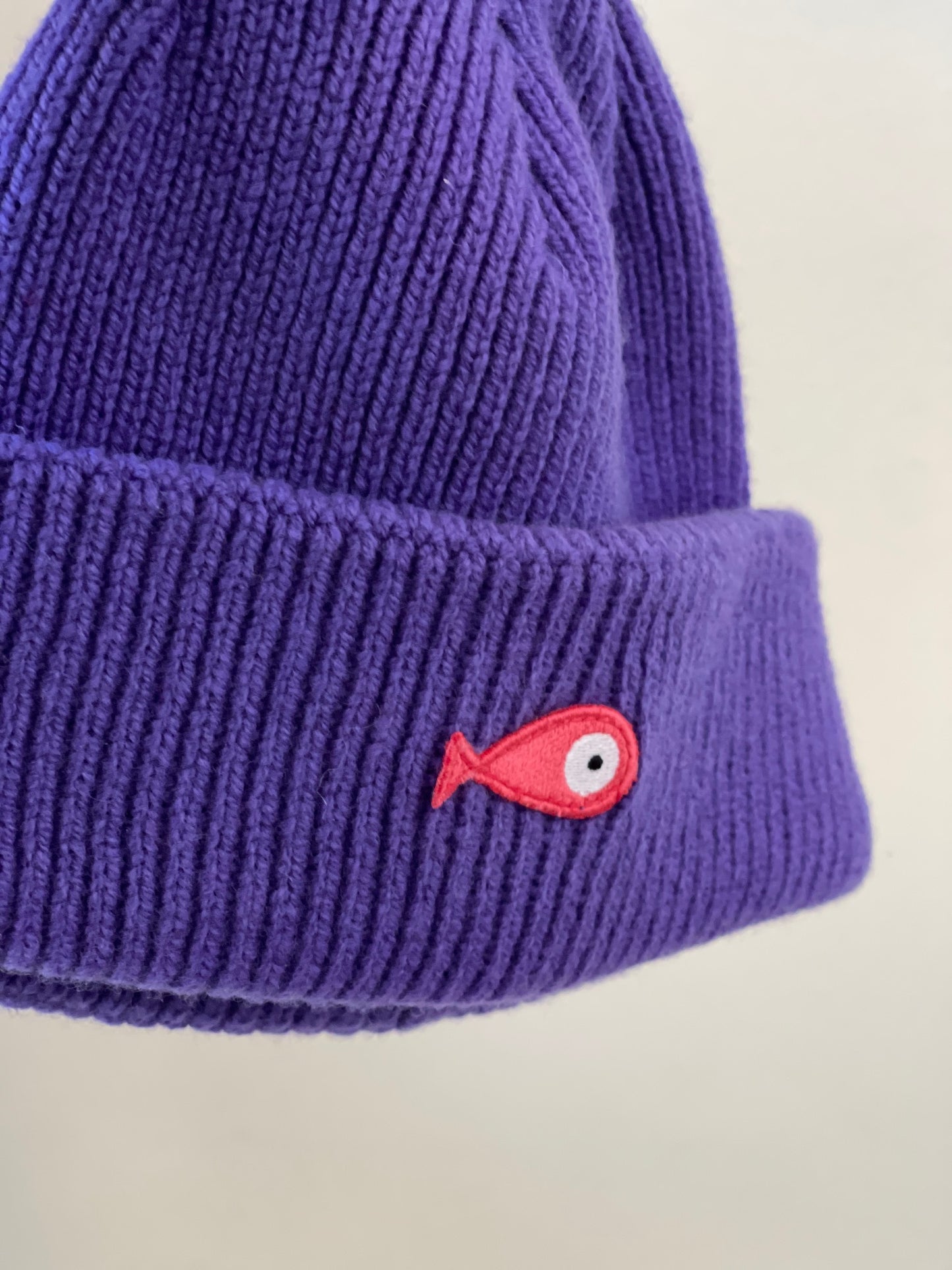 The soft, colorful, and warm kids/baby beanies crafted from luxurious lambswool yarn.   Adorned with a playful fish patch for a touch of playfulness. ( The Turquoise color features a distinctive back label. The front of the label showcases a pink fish, turn the label around, and you'll find our logo discreetly placed on the back )  Vibrant palette of seven colors – Yellow, Purple, Red, Blue, Pink, Navy Blue and Turquoise. Detail
