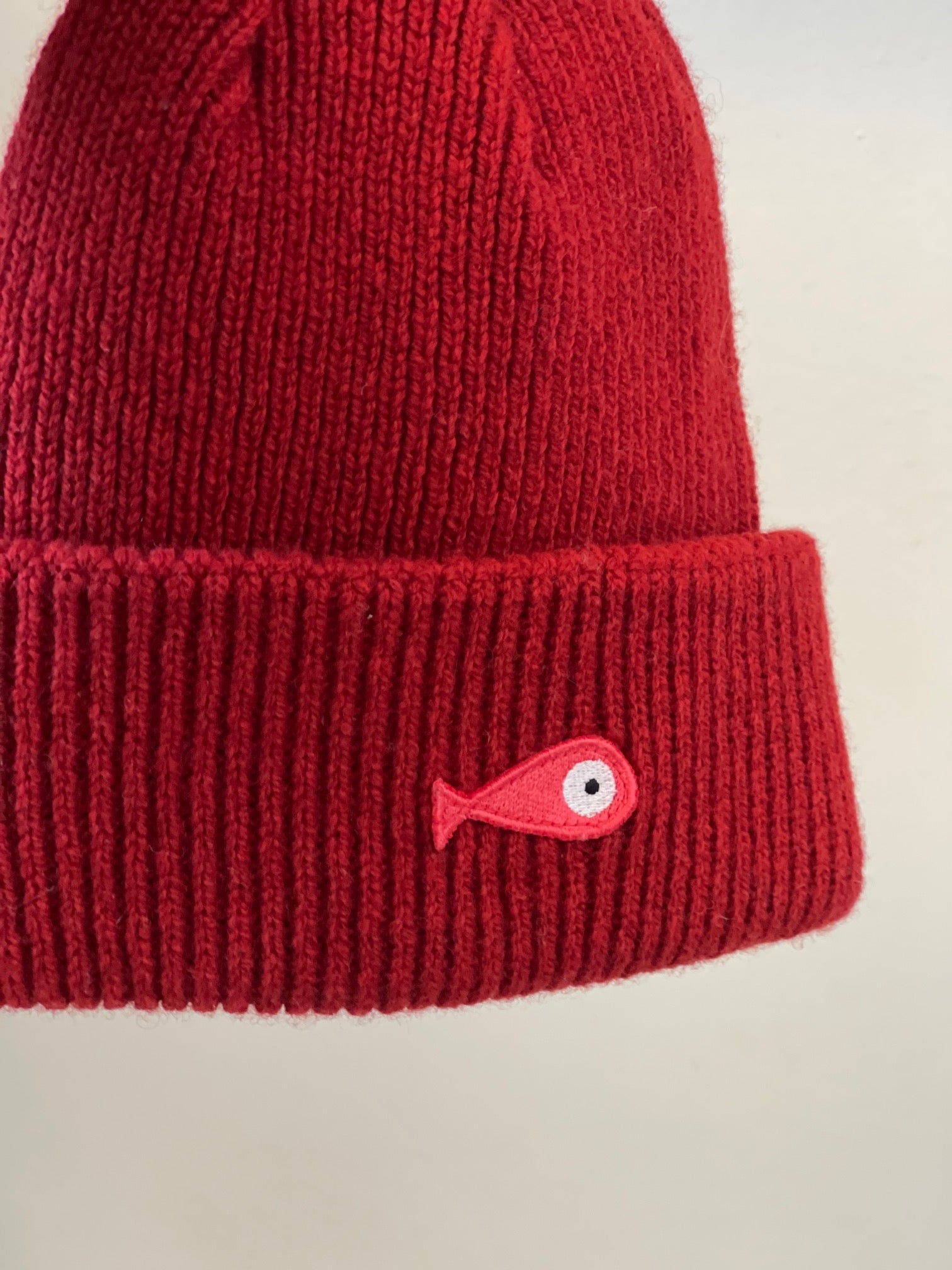 The soft, colorful, and warm kids/baby beanies crafted from luxurious lambswool yarn.   Adorned with a playful fish patch for a touch of playfulness. ( The Turquoise color features a distinctive back label. The front of the label showcases a pink fish, turn the label around, and you'll find our logo discreetly placed on the back )  Vibrant palette of seven colors – Yellow, Purple, Red, Blue, Pink, Navy Blue and Turquoise. Detail