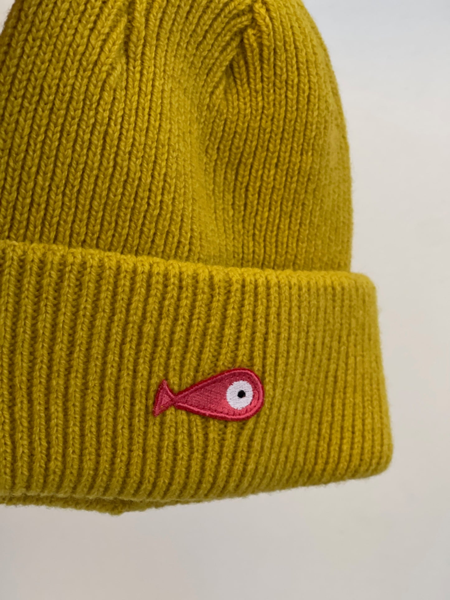 The soft, colorful, and warm kids/baby beanies crafted from luxurious lambswool yarn.   Adorned with a playful fish patch for a touch of playfulness. ( The Turquoise color features a distinctive back label. The front of the label showcases a pink fish, turn the label around, and you'll find our logo discreetly placed on the back )  Vibrant palette of seven colors – Yellow, Purple, Red, Blue, Pink, Navy Blue and Turquoise.