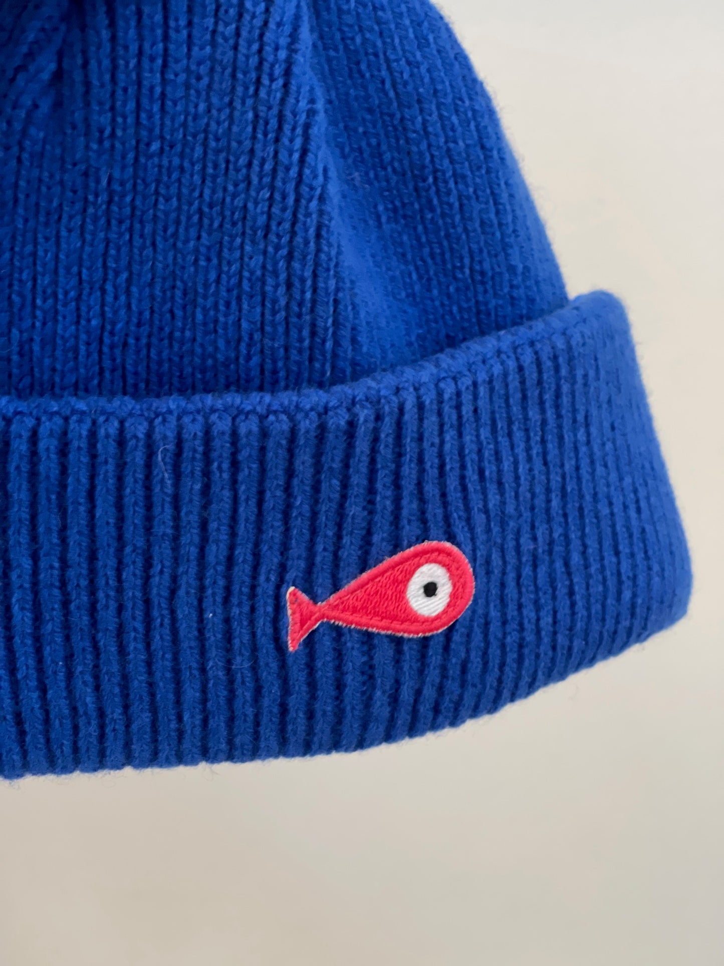The soft, colorful, and warm kids/baby beanies crafted from luxurious lambswool yarn.   Adorned with a playful fish patch for a touch of playfulness. ( The Turquoise color features a distinctive back label. The front of the label showcases a pink fish, turn the label around, and you'll find our logo discreetly placed on the back )  Vibrant palette of seven colors – Yellow, Purple, Red, Blue, Pink, Navy Blue and Turquoise. Detail