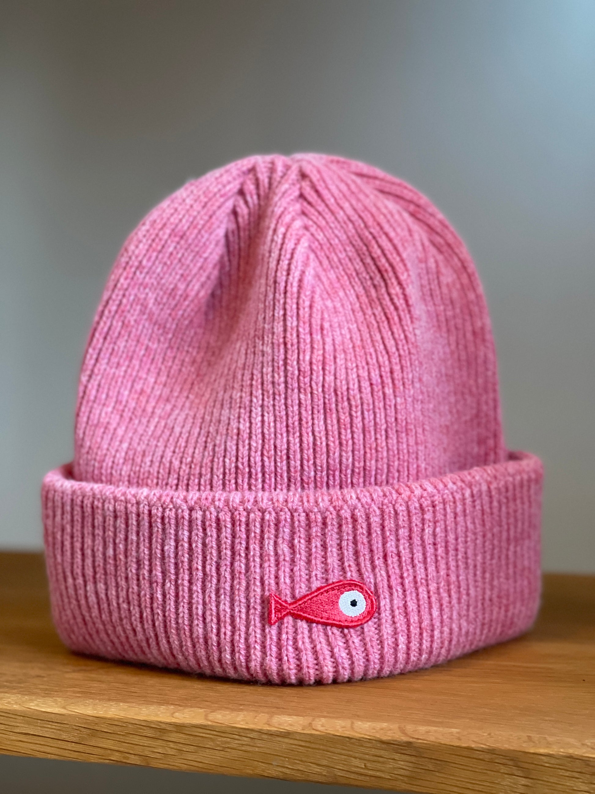 The collection of soft, colorful, and warm beanies crafted from luxurious lambswool yarn. Embrace comfort and style with these lovely accessories available in four captivating colors: Pink, Blue, Vibrant Mint, and Light Grey. Each beanie features a unique fish patch, adding a touch of charm and playfulness.  Front
