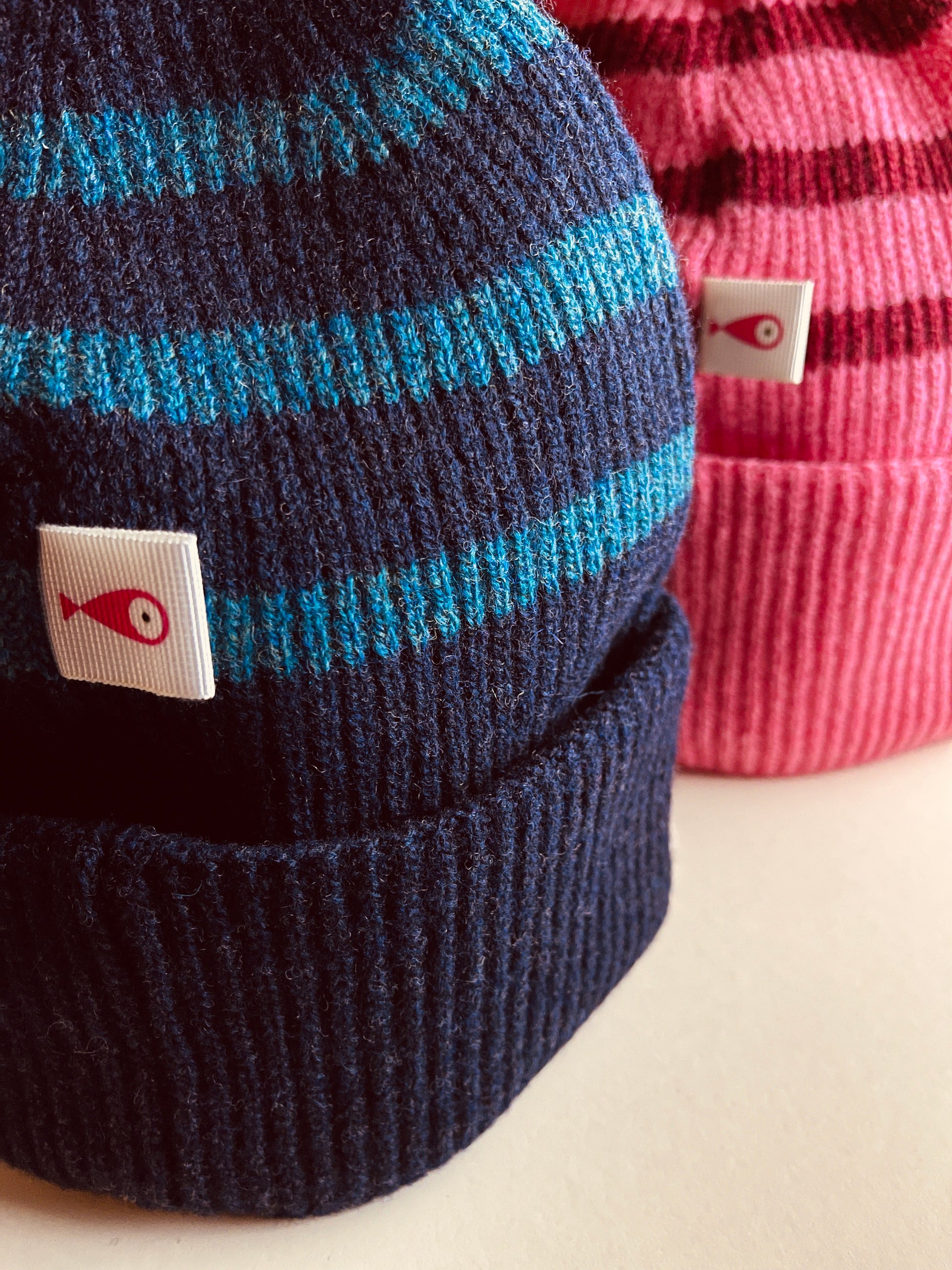 The collection of soft, colorful, and warm beanies crafted from luxurious lambswool yarn. Embrace comfort and style with these lovely accessories available in two lovely colors: Pink with red stripes and Navy blue with lighter blue stripes. Detail