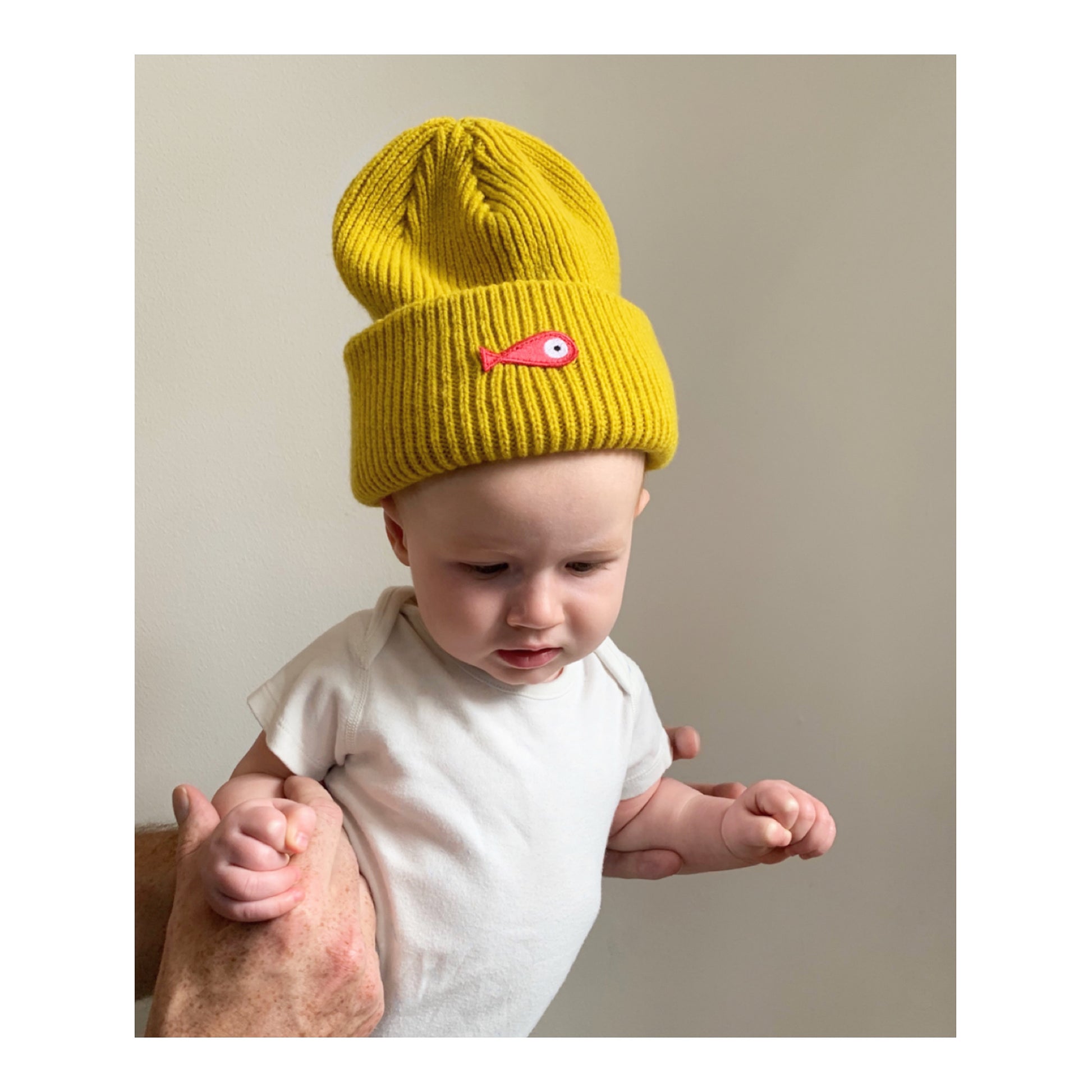 The soft, colorful, and warm kids/baby beanies crafted from luxurious lambswool yarn.   Adorned with a playful fish patch for a touch of playfulness. ( The Turquoise color features a distinctive back label. The front of the label showcases a pink fish, turn the label around, and you'll find our logo discreetly placed on the back )  Vibrant palette of seven colors – Yellow, Purple, Red, Blue, Pink, Navy Blue and Turquoise. Front
