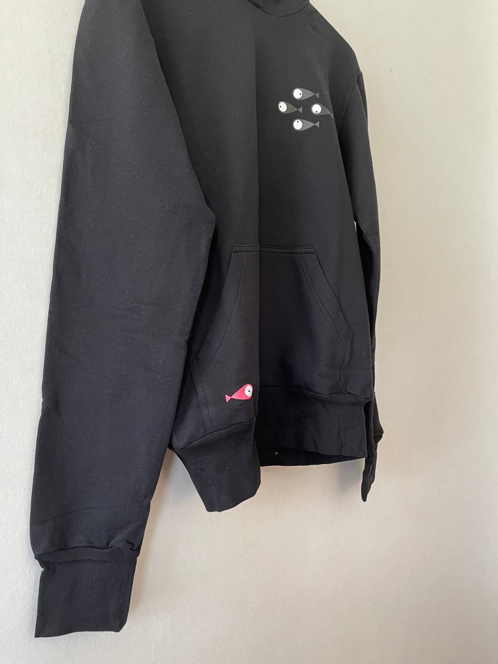 Super cozy hoodie with a kangaroo pocket in the front with no drawstrings. Crafted from 100 % superfine cotton. Raglan sleeves, ribbed trims. The pieces have a pink fish print on front left bottom corner and 4 black fishes print on right chest side.    Colour: black Material: 100% cotton