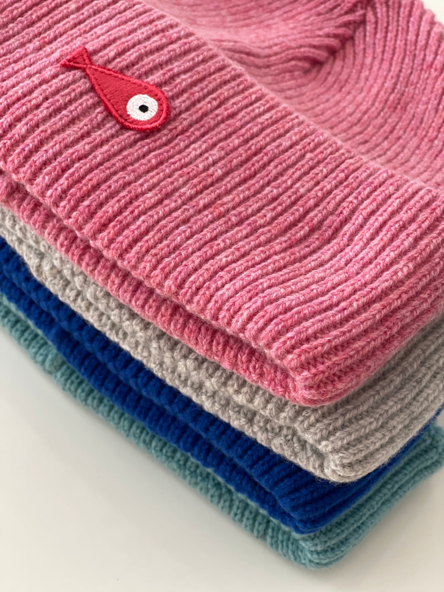 The collection of soft, colorful, and warm beanies crafted from luxurious lambswool yarn. Embrace comfort and style with these lovely accessories available in four captivating colors: Pink, Blue, Vibrant Mint, and Light Grey. Each beanie features a unique fish patch, adding a touch of charm and playfulness.  Detail