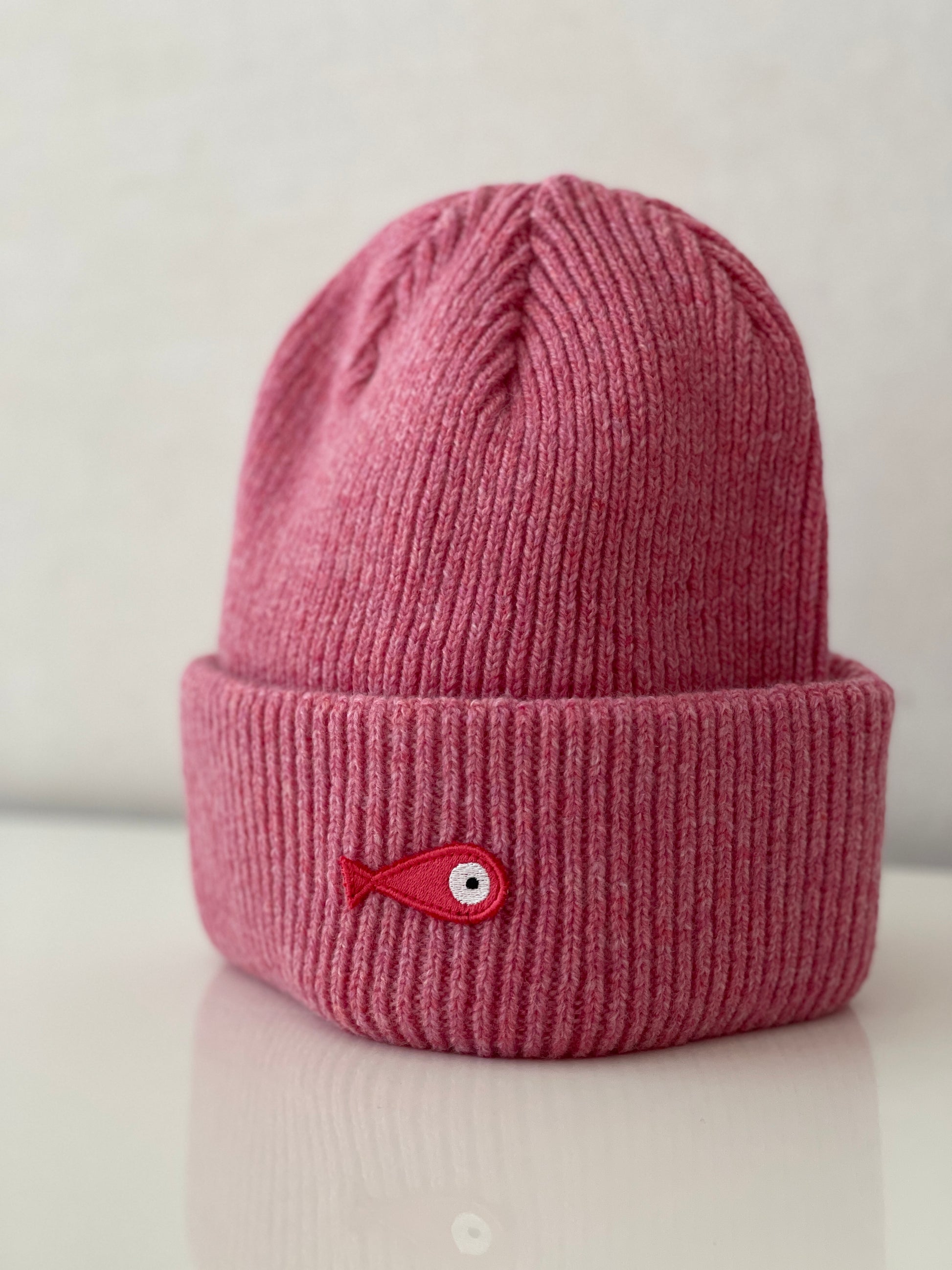 The collection of soft, colorful, and warm beanies crafted from luxurious lambswool yarn. Embrace comfort and style with these lovely accessories available in four captivating colors: Pink, Blue, Vibrant Mint, and Light Grey. Each beanie features a unique fish patch, adding a touch of charm and playfulness.  Front