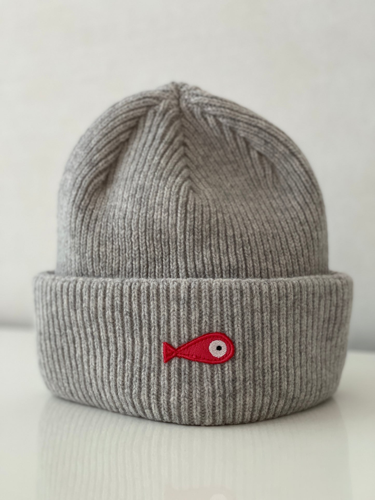 The collection of soft, colorful, and warm beanies crafted from luxurious lambswool yarn. Embrace comfort and style with these lovely accessories available in four captivating colors: Pink, Blue, Vibrant Mint, and Light Grey. Each beanie features a unique fish patch, adding a touch of charm and playfulness.  Front